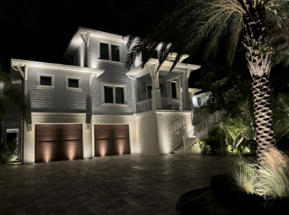 Coastal home with 3-car garage and architectural LED uplighting with paver driveway at night